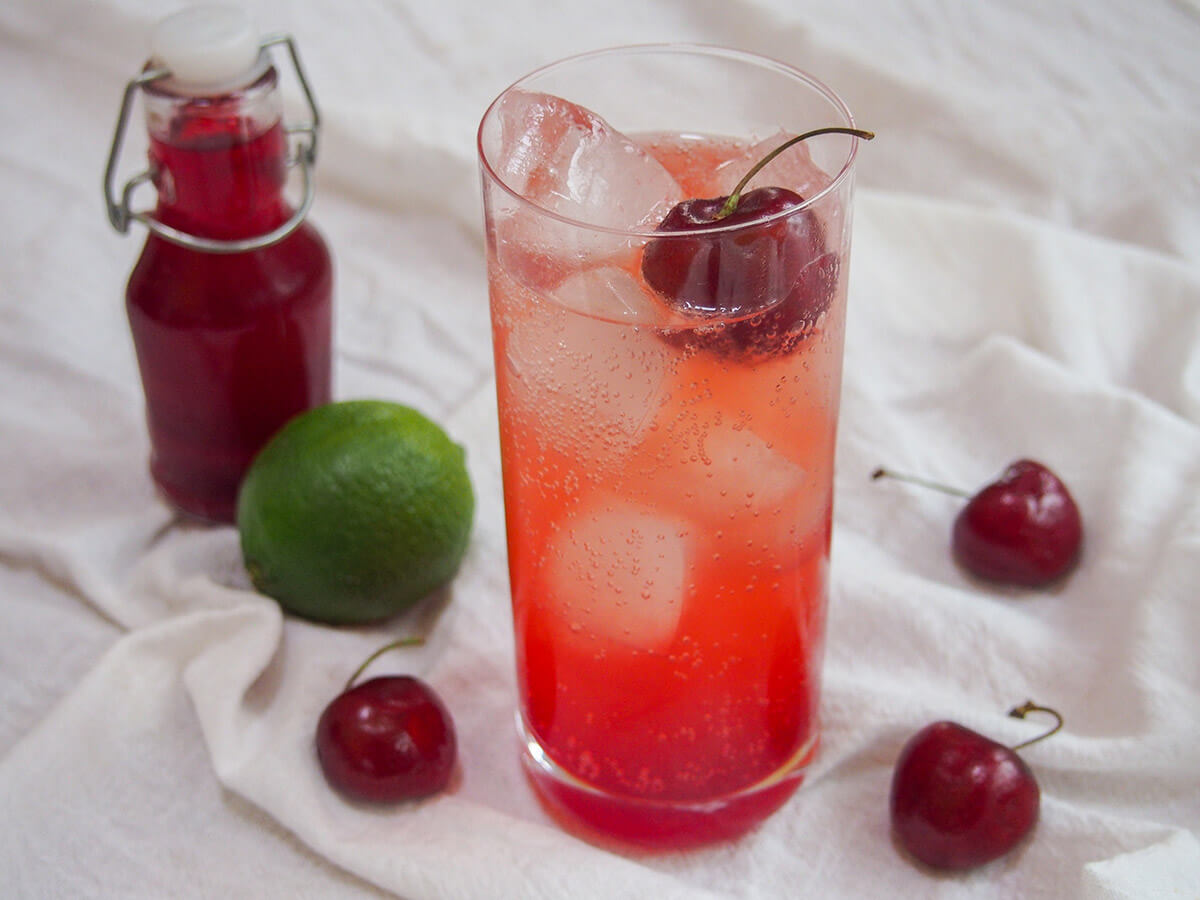 glass of Shirley Temple drink with lime and bottle of grenadine behind