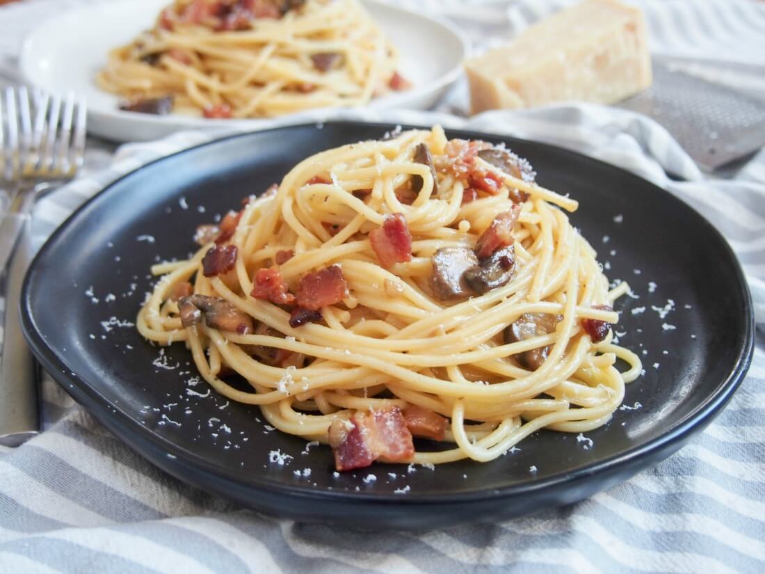 Spaghetti alla carbonara with mushrooms on plate with forks to side and another plate behind