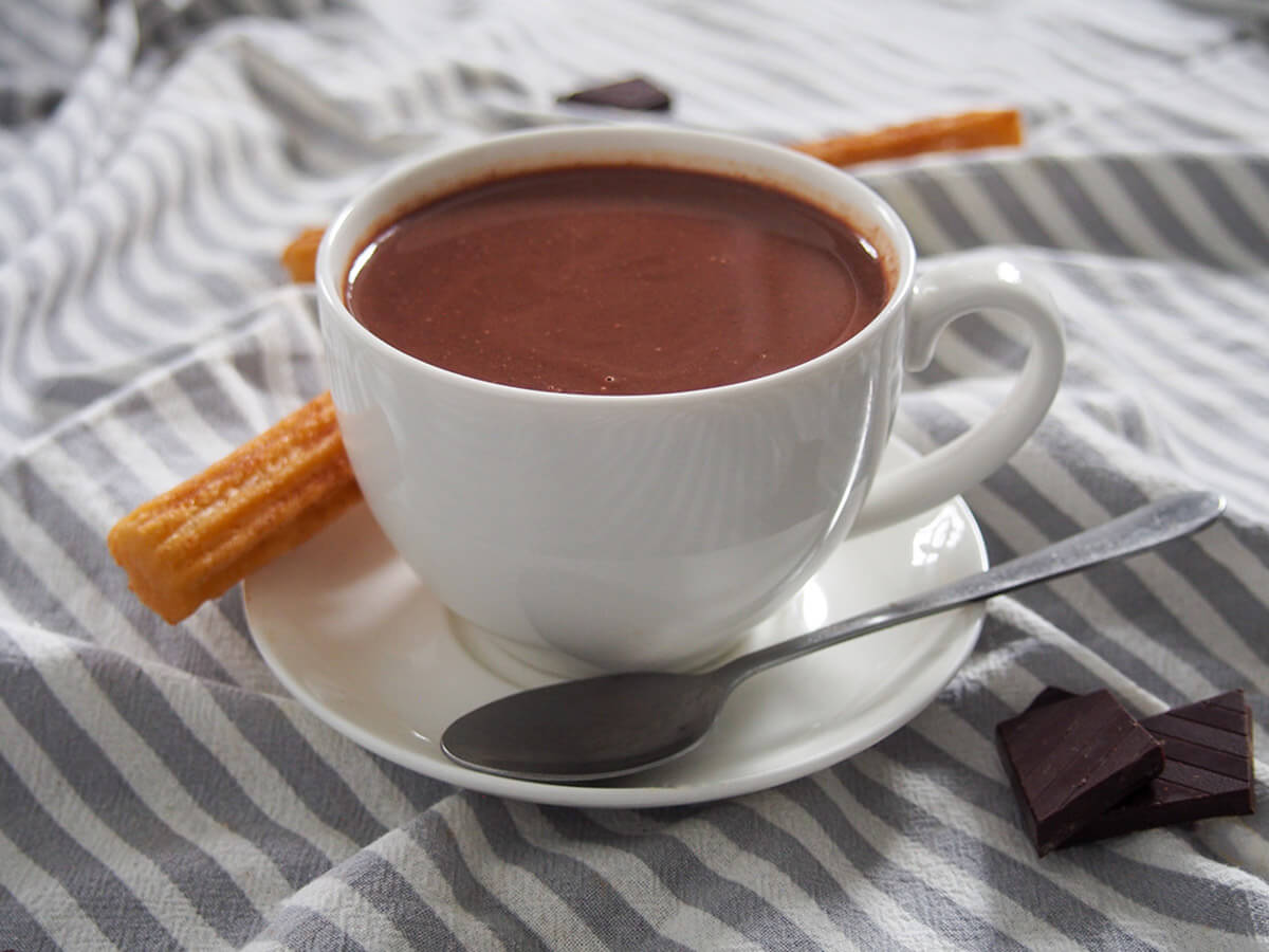 cup of Spanish hot chocolate with spoon in front and churro behind