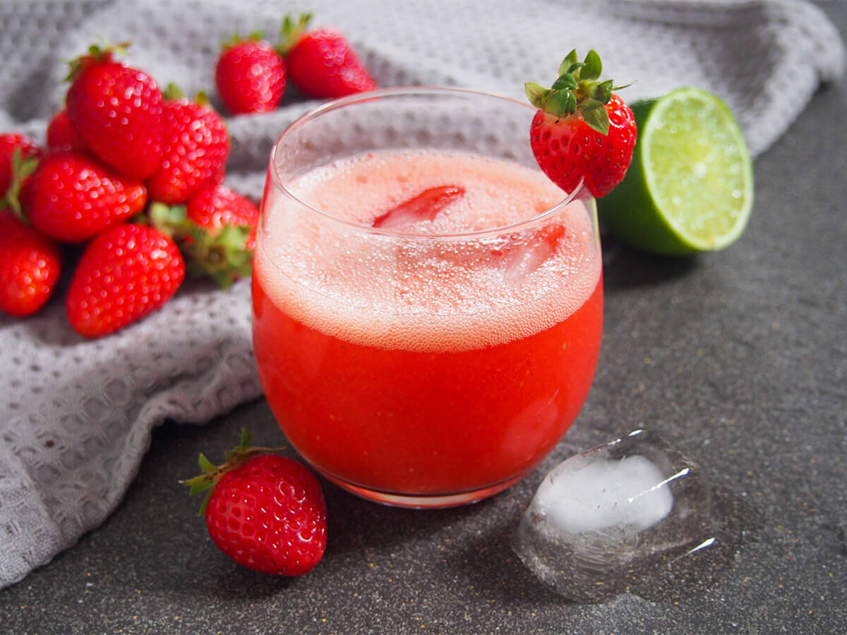 glass of strawberry agua fresca with strawberries to one side and half lime to other