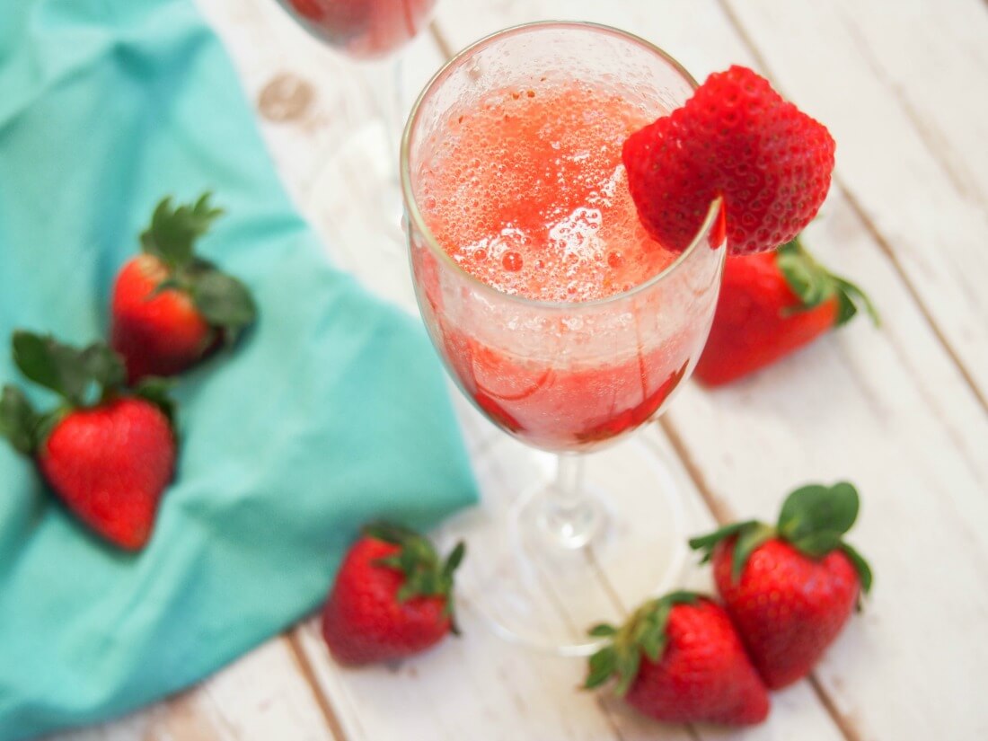 glass of strawberry bellini with strawberries to side