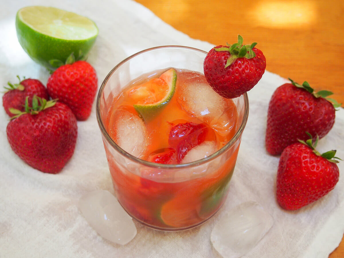 glass of strawberry caipirinha with strawberries either side and half lime on left