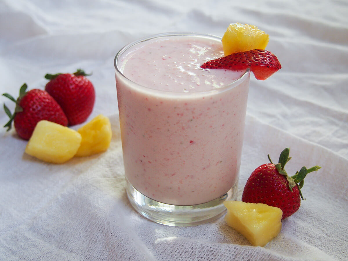 glass of strawberry pineapple smoothie with fruit to side