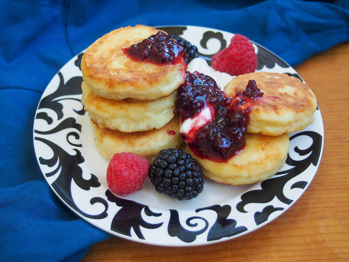 plate of syrniki Russian cheese pancakes with jam, sour cream and fruit