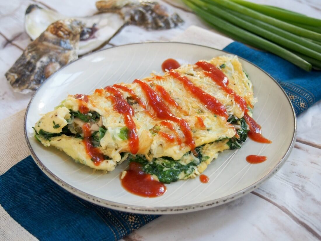 Taiwanese oyster omelette on plate with oyster shells and scallions behind